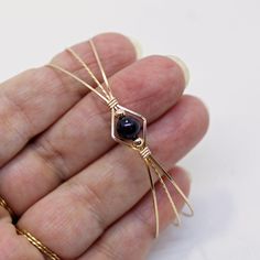 a hand holding a tiny gold and black beaded spider brooch with an amethorate stone