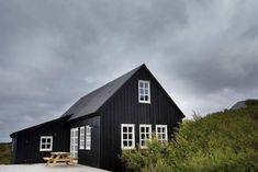 a black house sitting on top of a lush green hillside next to a wooden bench