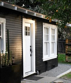 a small black house with white doors and windows next to a planter filled with succulents