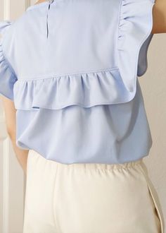 "Fresh as a breath of spring, the Hana ruffle blouse will be your perfect warm-weather wardrobe essential. This relaxed ruffle tunic top is crafted in a lightweight organic cotton fabric with an uplifting and serene sky blue colour that will never go out of style. Blending classic and contemporary style with attention-grabbing accents such as a detailed bib with romantic ruffles, this eco-friendly top will create endless opportunities for your wardrobe. Perfect for just hanging out at home or go Brunch Tops With Ruffle Hem And Ruffled Collar, Spring Tops With Ruffle Hem And Ruffled Collar, Spring Blouse With Ruffle Hem For Work, Spring Workwear Blouse With Ruffle Hem, Elegant Blue Tops With Ruffle Hem, Spring Ruffled Tops For Brunch, Spring Brunch Tops With Ruffles, Feminine Solid Tops For Spring, Feminine Tops With Ruffle Hem For Work