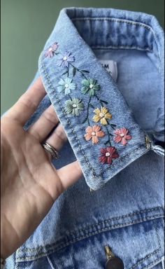 someone is holding up a jean jacket with flowers on it