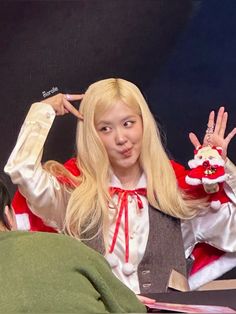 a woman dressed as santa clause holding her hands up in the air while sitting at a desk