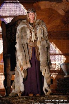 a woman in a fur coat standing next to a chair