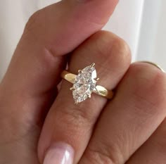 a woman's hand holding a yellow gold ring with two pear shaped diamonds on it