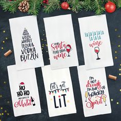 six hand - lettered christmas tea towels on a table with pine cones and decorations