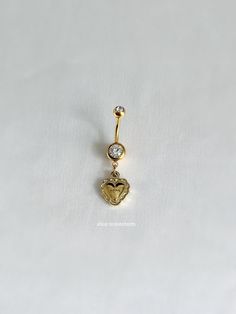 a gold heart shaped belly ring with a diamond in the center on a white background