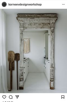 an old mirror is in the middle of a white room with wooden utensils