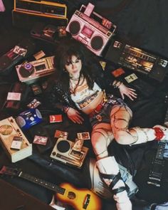 a woman laying on top of a bed with lots of items around her and an electric guitar