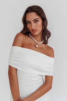 a woman wearing a white dress and pearl necklace, posing for the camera with her hands on her hips