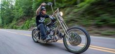 a man riding on the back of a motorcycle down a curvy road with trees in the background