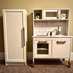 a toy kitchen with a refrigerator, sink and cupboard in the corner on carpeted flooring