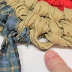 a hand is pointing at two different colored scarves on a white surface, one with a red and blue plaid design