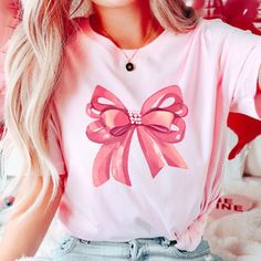 Embrace elegance and flirtatious charm with our captivating pink bow shirt, a delightful addition to your coquette-inspired wardrobe! 🌸👚 This shirt embodies the essence of femininity and playfulness, perfect for those who adore a touch of chic sophistication with a hint of flirtation. 🌷 The darling pink hue complements the shirt's design, accentuating the focal point--an exquisitely crafted oversized bow adorning the neckline or sleeves, adding a whimsical and flirtatious allure to your ensem Cute Bow T-shirt For Spring, Spring Party Tops With Ribbon, Feminine Pink Tops With Short Sleeves, Feminine Tops With Ribbon For Spring, Feminine Pink Short Sleeve Tops, Feminine Ribbon Tops For Spring, Cute Pink T-shirt With Bow, Pink Summer Party Shirt, Pink Casual T-shirt For Party