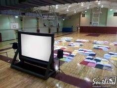 an empty basketball court with rows of squares on the floor and white screen in center