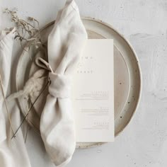 an empty plate with a napkin and some dried plants on it next to a white dinner cloth