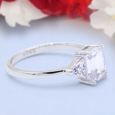 a white diamond ring sitting on top of a table next to red and white flowers