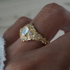 Step into a realm of ethereal beauty with our enchanting "Moonstone Moon Diamond" ring. This ring features a magical natural moonstone with a blue sheen when light reflects on it. Handcrafted in your choice of 14K and 18K gold. Only one available. All orders come in our Tippy Taste ring box. This ring is handmade and designed in NYC. 14K or 18K solid gold Natural oval moonstone. 6*4mm 12 Natural round diamonds. SI clarity, GH color, 0.11ct total carat weight 1.1mm width, 1.5mm thick band ** Tippy Taste Heirloom Collection is made to order. Please allow 3-4 week turnaround time. Shipping:Domestic: Free shippingInternational: Free shippingAll orders are insured, come with tracking, and with signature requirements. Please review our international shipping. Customization:- Interested in custom Moonstone Engagement Ring Gold, Moonstone Ring Engagement, Celestial 14k Gold Opal Wedding Ring, Celestial Moonstone Ring With Rose Cut Diamonds, Celestial Moonstone Rings With Rose Cut Diamonds, Celestial Moonstone Ring For Wedding, Celestial Moonstone Wedding Ring, Gold Celestial Moonstone Ring In 14k, Gold Moonstone Ring With Moon Phase For Wedding