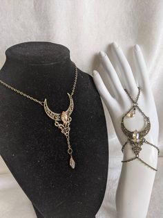 A beautiful and unique jewelry set which includes a pendant necklace and hand chain, featuring a filigree moon and connector charm with a crystal decorating the center of the moon and a drop crystal hanging from the pendant. Choose Crystal Shape between horse eye (as pictured) or teardrop (horse eye will be sent if unspecified) Choose necklace length from the diagram in the listing picture (14 inches plus 1.5 inch extension chain will be sent if unspecified) Crescent Moon Charm Jewelry For Parties, Crescent Moon Charm Party Jewelry, Moon Charm Pendant Jewelry For Party, Party Pendant Jewelry With Moon Charm, Party Moon Charm Pendant Jewelry, Elegant Moonstone Jewelry For Festivals, Fantasy Moon Shaped Jewelry Gift, Gothic Festival Jewelry With Moon Charm, Fantasy Silver Jewelry With Moon Charm