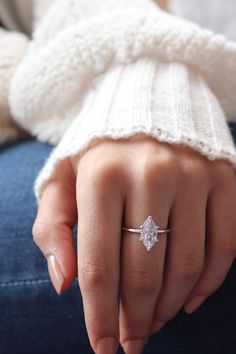 a woman's hand with a diamond ring on her left finger, wearing a white sweater