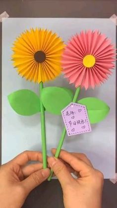 someone is holding two paper flowers in front of a piece of paper that says, happy mother's day