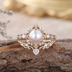 a pearl and diamond ring sitting on top of a piece of wood with flowers in the background