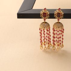 Description: These jhumki earrings from Tarinika are a classic piece with a statement yet simple style. It showcases polki stones set on a floral arrangement having a jhumki drop with beads chain on a gold-plated base. The beaded chains and the minimal design add to its sophistication and richness. Details & Specifications: Materials used: Brass Alloy with Yellow Gold Plating Weight - Earrings 29.13 gm Length - Earrings 9 cm Make it custom Want to make it a custom earring? Sure! Reach out to us Elegant Gold Jhumkas With Dangling Beads, Traditional Gold Jhumkas With Dangling Beads, Traditional Red Chandbalis Drop Earrings, Elegant Red Ruby Jhumkas, Gold Ruby Chandbali Chandelier Earrings, Buy Jewellery Online, Jhumki Earrings, Beads Chain, Indian Jewellery Design