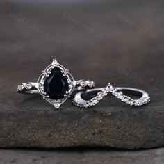 two wedding rings with black diamonds on top of them, sitting on a stone slab