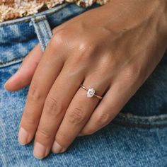 a woman's hand with a diamond ring on her left hand, wearing blue jeans