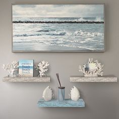 two white shelves with sea shells on them in front of a painting and bookshelf