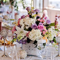 a vase filled with lots of flowers sitting on top of a table next to wine glasses