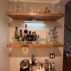 two wooden shelves filled with liquor bottles and glasses on top of a counter next to a sink