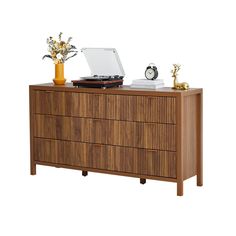 a record player sitting on top of a wooden dresser next to a vase with flowers