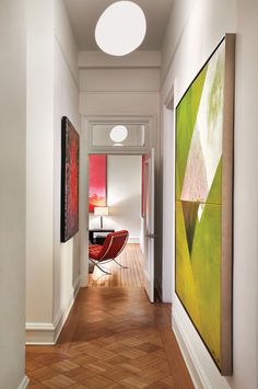 a hallway with two paintings on the wall and a red chair in the corner next to it