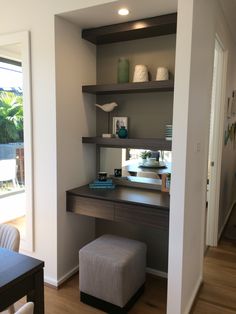 a desk and chair in a room with open shelves on the wall above it, along with a footstool