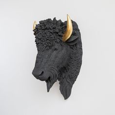 a black bull head with gold horns on it's face is shown against a white wall