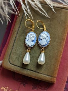 "Absolutely lovely, these peach cameo earrings are perfect for a Gothic or Historical period wedding! They would make an excellent gift for anyone that loves vintage-style jewelry. Featuring golden brass lace-edged bezel settings mounted with blue and white portrait cameos. Adorned with an elegant, teardrop shaped ivory glass pearl.  *Please note: the settings sometimes may have random designs on the back, this is common from processing and not noticeable while wearing. Size: Suspended by hook e Cameo Drop Earrings Jewelry Gift, Cameo Drop Earrings As Gift, Gift Cameo Drop Earrings Jewelry, Elegant Cameo Earrings, Cameo Round Earrings As Gift, Cameo Drop Earrings For Wedding, Cameo Earrings For Gift, Elegant Cameo Earrings As Gift, Elegant Cameo Earrings For Gift