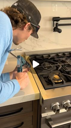 a woman is using a drill to fix a stove top burner in a kitchen