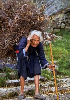 an old woman is leaning on a pole and holding a broom in her hand while she looks at the ground