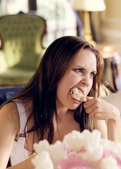 a woman sitting at a table with food in her mouth and eating something out of her hand