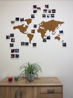 a wooden dresser topped with a potted plant next to a wall covered in photos