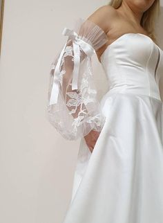 a woman in a white wedding dress with a veil on her shoulder and an arm