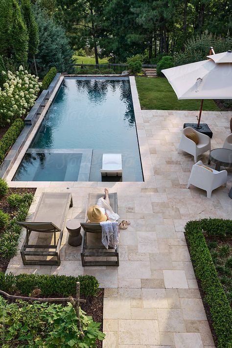 A serene property with forest view, garden, lake, and pool in idyllic setting. Woman relaxes poolside with a book on a lounge chair in the summer. Garden Design With Swimming Pool, Entertaining Pool Area, Landscaping With Pool Backyard, Midwest Pool Landscaping, Pool In The Garden, Pool House Pergola, Pavers Backyard Pool, Pool Landscaping Design, Pool Near House