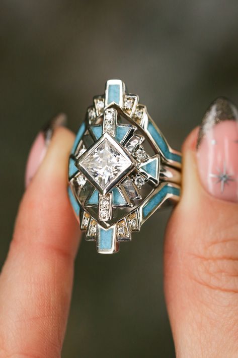 A close-up image of a woman's fingers holding a "Calliandra" design three-piece wedding ring set from Staghead Designs. This ring set features geometric Western-style design elements & a 2ct princess cut moissanite engagement ring with crushed turquoise inlays & diamond accents & is paired with two matching turquoise & diamond bands. This ring is shown in 14K white gold but can also be made in yellow or rose gold. Western Wedding Ring Stacker, Engagement Rings With Unique Stones, Unique Turquoise Rings, Navajo Wedding Rings, Turqouise Wedding Ring, Southwestern Engagement Ring, Native Wedding Rings, Southwest Engagement Ring, Tourquise Wedding Rings