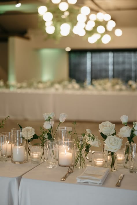 This beautiful wedding took place at Casita Hollywood, a Los Angeles wedding venue. It featured white flowers in bud vases along with pillar candles and votive candles flowing down the table. Each table was draped in white linens giving the space a clean and classic look. Photo: Karina Santos Photography | Florist: La Petit Gardenia Classic White Wedding Table Setting, Simple White Reception Decor, Candles And Flowers Table Setting, Wedding Florals Long Table, Gardenia Centerpiece Wedding, Blush Floral Arrangements Wedding, Bud Vases And Pillar Candles Wedding, White Flower Candle Centerpieces, Candle Based Centerpieces