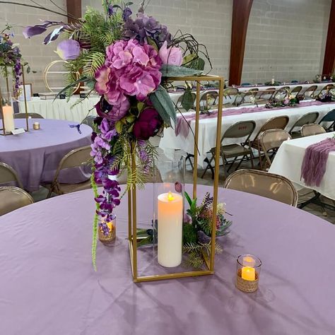 Brighten up your wedding tablescapes with chic table centerpieces and ooze magical flair all around. Dress up the tables in lavender tablecloth and create a visually appealing effect of height and dimension by setting gold flower stands decorated with a purple & lavender hued hydrangea, peonies, orchid stems, wisteria vines, & greenery spray flower arrangement. Highlight the majestic appeal of your tablescape by arranging LED pillar candles and votive candles in honeycomb base candle holders. Wisteria Table Decorations, Gold And Purple Centerpieces, Purple And Gold Table Setting, Wisteria Centerpiece, Lavender Centerpieces, Wisteria Vines, Tangled Wedding, Gold Table Setting, Purple Centerpieces