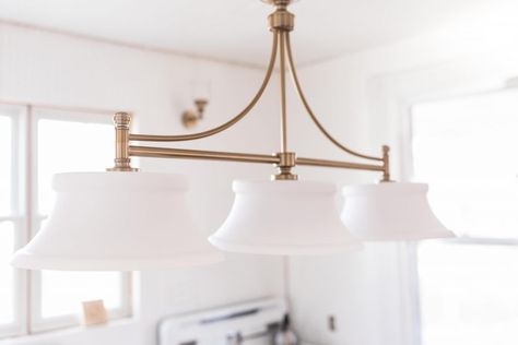 beautiful brass light fixture with three glass lamps in a victorian farmhouse Update Farmhouse, Chandelier Over Island, Victorian Farmhouse Kitchen, Victorian Light Fixtures, Farmhouse Kitchen Light Fixtures, Vintage Farmhouse Sink, Updated Victorian, Kitchen Light Fixtures, Vintage Shelving