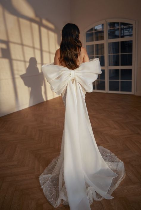 F/W2023 Collection, Love Poem, the Glow wedding dress is a feminine sparkly fitted gown. Features a long skirt and a sweetheart corset with semi sheer side cuts. Includes a dramatic pleated overskirt and detachable shoulder straps. Optional unique oversized bow cape. #leegrebenau #luxuryweddingdress #luxurywedding #ballgown #bridaltrends2023 #weddingdress Wedding Dresses Bow, Fashion Forward Wedding, Spring Wedding Dresses, Dresses Bow, Cape Wedding, Spring Wedding Guest Dress, Cape Wedding Dress, Bow Wedding Dress, Spring Wedding Dress