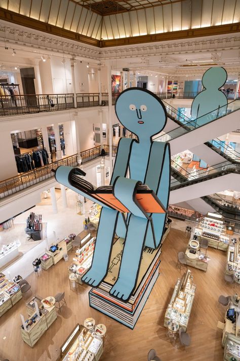 Inside a department store with multiple levels, and large blue character towers all other objects, as it sits and reads a book Jean Jullien, Pop Up Cafe, Paris Store, Paper People, Caran D'ache, Store Windows, Modern Crafts, Tokyo Travel, Rive Gauche