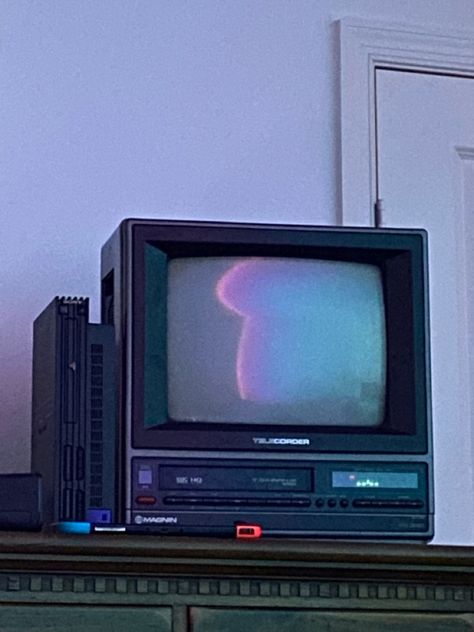 An 80s tube tv sitting on a wooden dresser, the screen is off and the reflection shows cool colored lights in the room. Next to it is a ps2, in front of it is a switch Old Tv Wallpaper, Tv Asthetic Picture, 2000s Tv Aesthetic, Old Television Aesthetic, 90s Tv Set, Games To Install On Your Phone, 80s Tv Aesthetic, Box Tv Aesthetic, Crt Tv Aesthetic