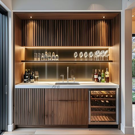 Explore this sleek modern home wet bar featuring a built-in wine cabinet with walnut wood slats, white marble countertop, and stainless steel sink. Warm LED lighting highlights glass shelves and wine glasses, set against light gray walls. The open design includes floor-to-ceiling windows and minimalistic decor, perfect for entertaining. Modern Bar House Design, Built Coffee Bar, Flip Up Bar Counter, Mcm Wet Bar, Wet Bar Cabinet With Sink, Small Basement Bar Ideas Modern, Modern Small Bar Ideas For Home, Modern Home Bar Luxury, Modern Wet Bar Ideas